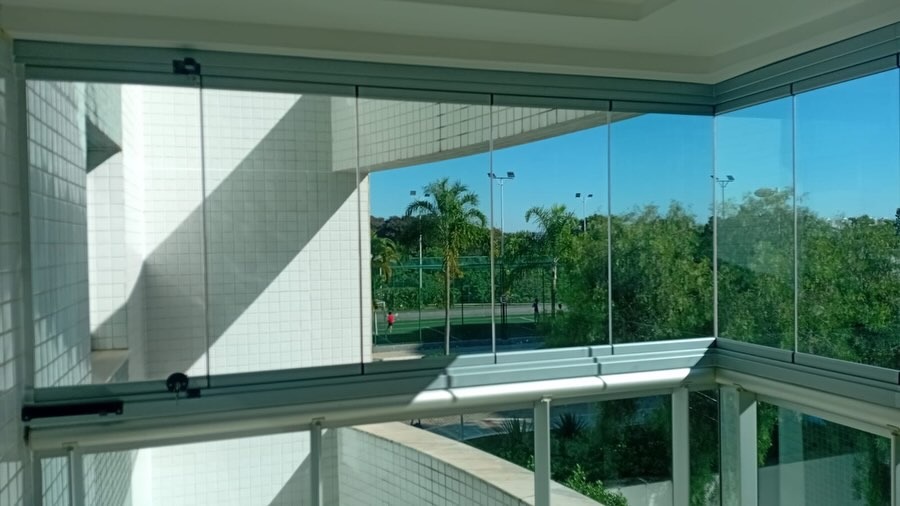 Varanda em canto envidraçada com vista para área verde do condomínio