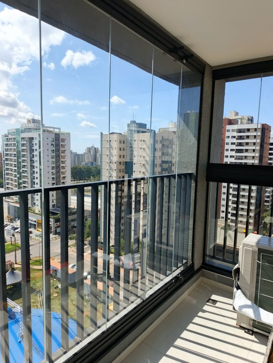 Varanda envidraçada com trilho superior aparente e vista para torres residenciais